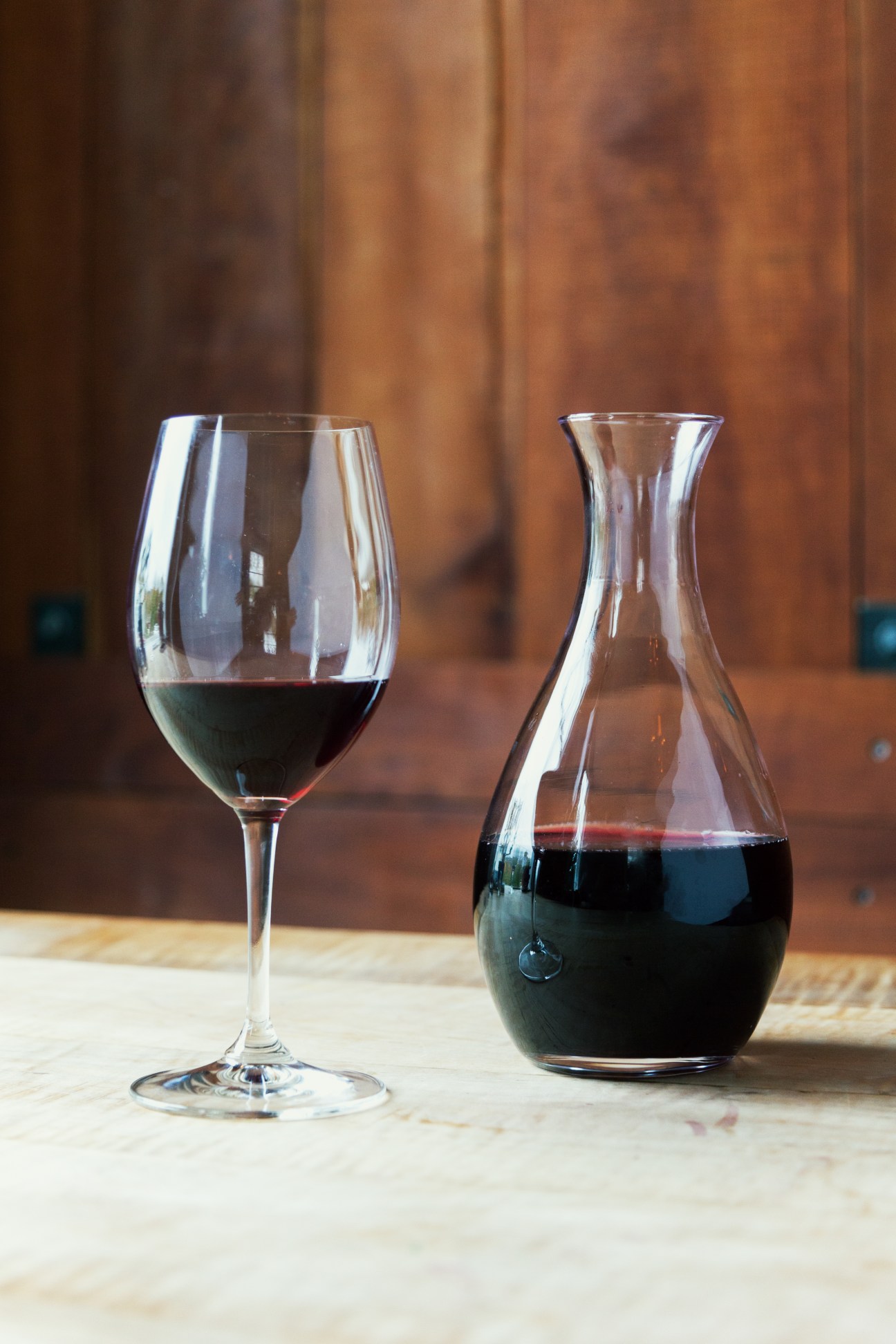 A glass of red wine and a decanter of Les Champs Libres crozes-hermitage wine on a wooden table.