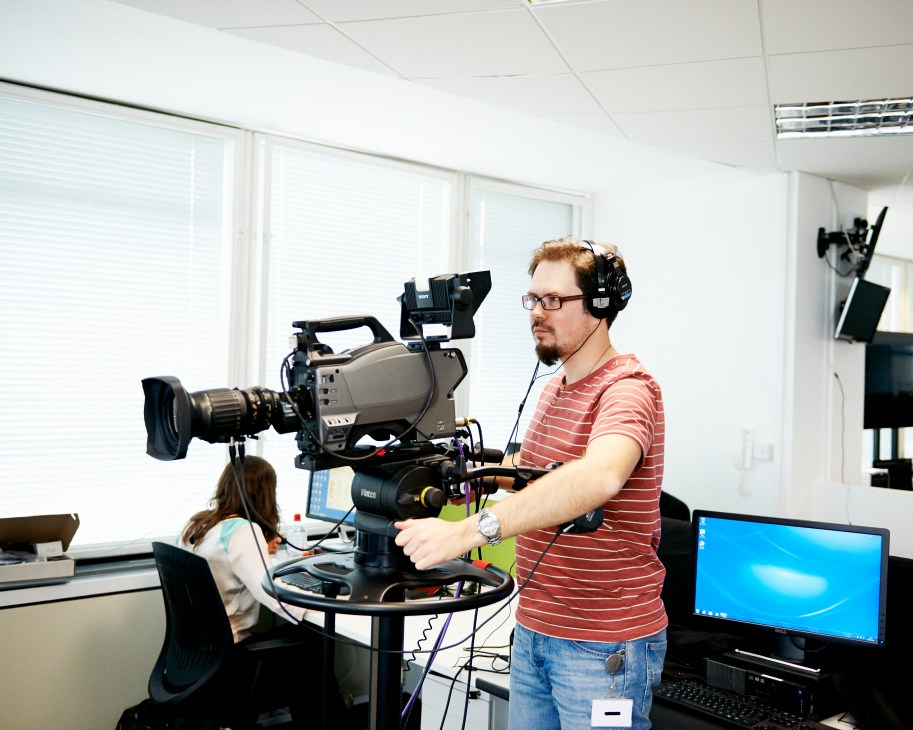 Cameraman in striped shirt operating professional video camera in bright studio at RT's London studios.