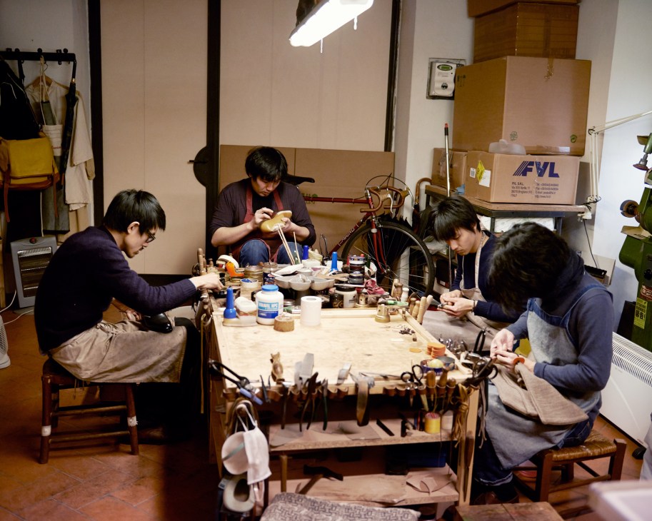 Three Japanese shoemakers working at a wooden workbench with tools in a Florence workshop.