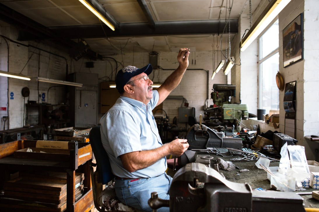 Eric Stones, a skilled craftsman at Ernest Wright & Son, stands at his workbench in the workshop surrounded by tools and scissor-making equipment.