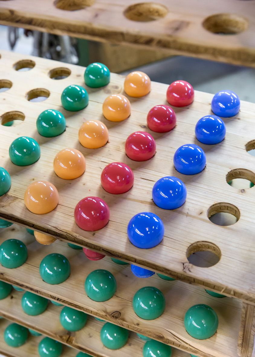 Colorful incandescent bulb domes arranged on wooden trays with holes, showing green, orange, red and blue varieties.
