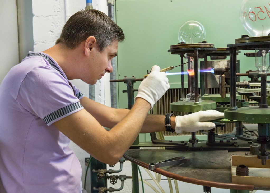 A worker in white gloves carefully handles a glowing incandescent bulb during manufacturing at Righi Licht.