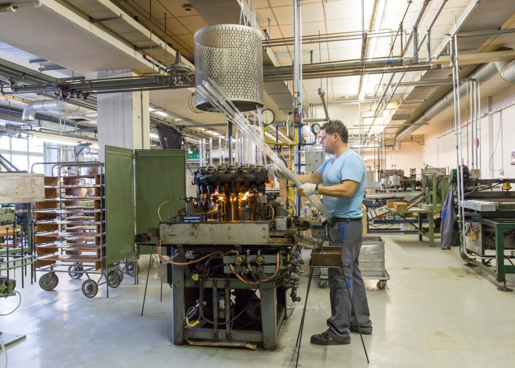 Worker operates vintage green machinery heating incandescent bulbs on a carousel in the Righi Licht factory.