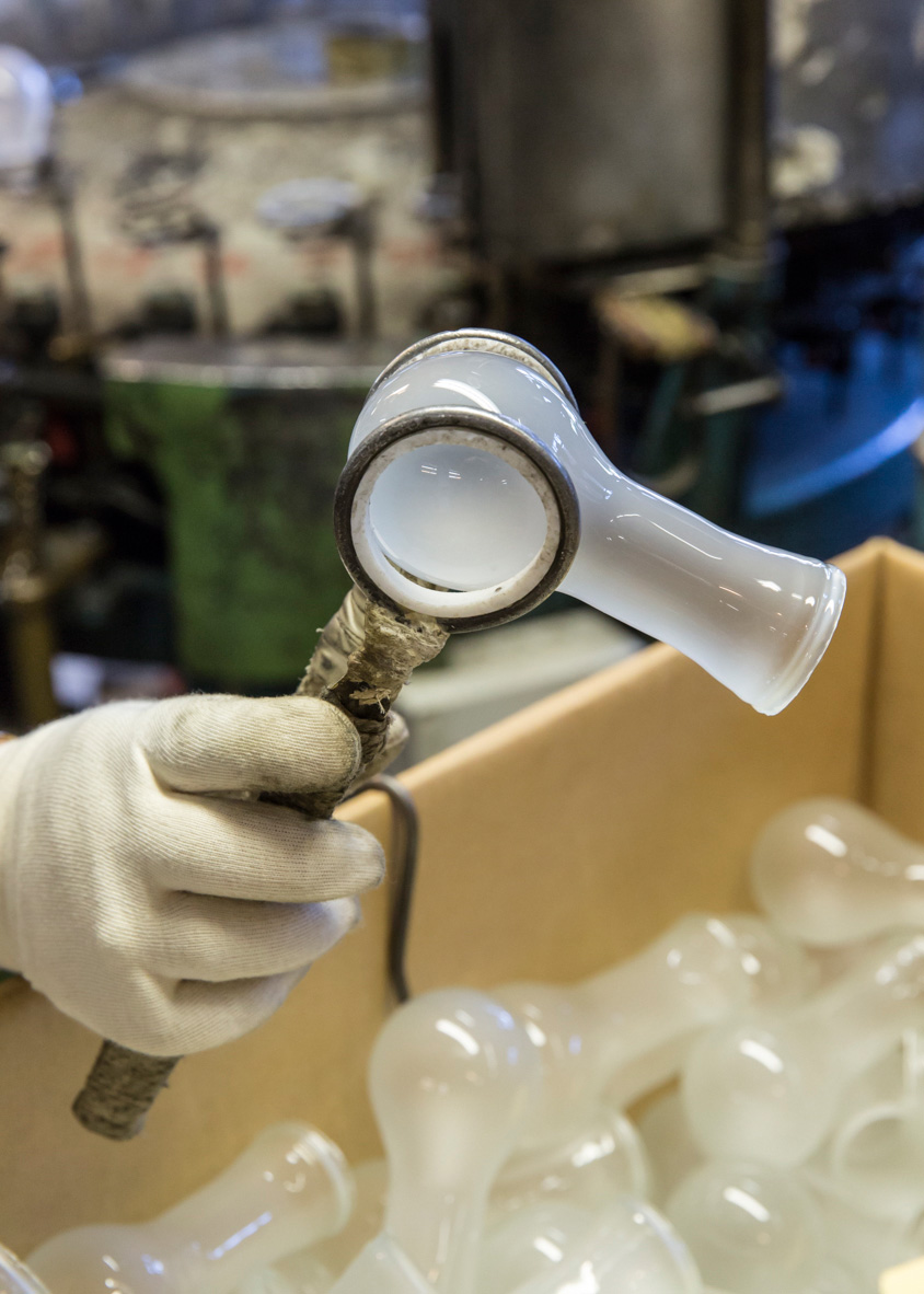 A gloved hand holding a delicate incandescent light bulb with visible tungsten filament and metal base.
