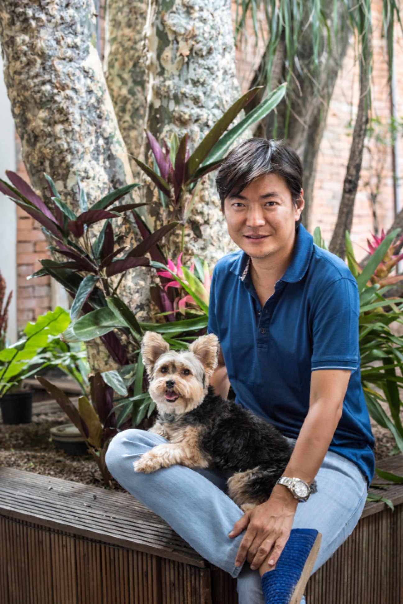 Landscape designer Alex Hanazaki posing with a small dog among tropical plants and trees.