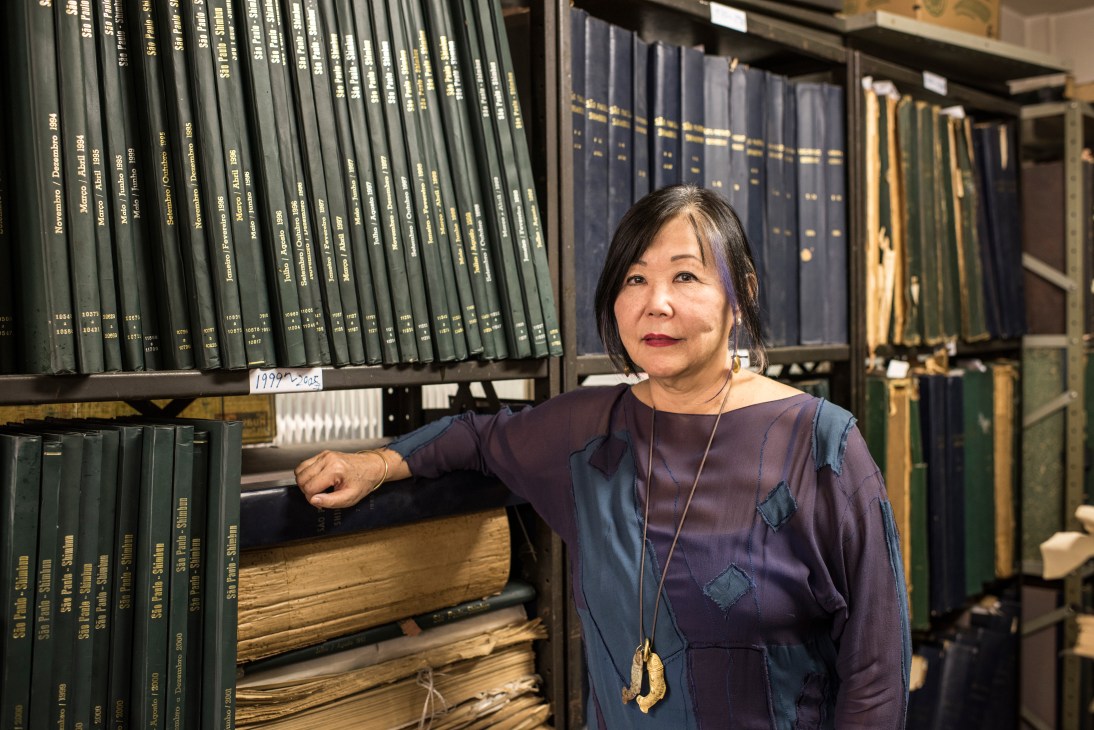 Helena Mizumoto stands beside shelves of bound Japanese-language newspapers at the São Paulo Shimbun office.