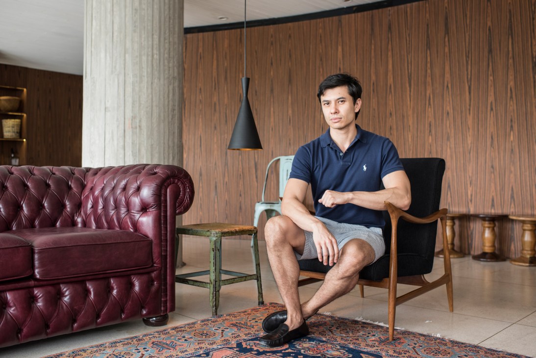 Food blogger Shoichi Iwashita sitting in a modern lounge area with wood paneling and contemporary furniture at Riviera Bar in São Paulo.