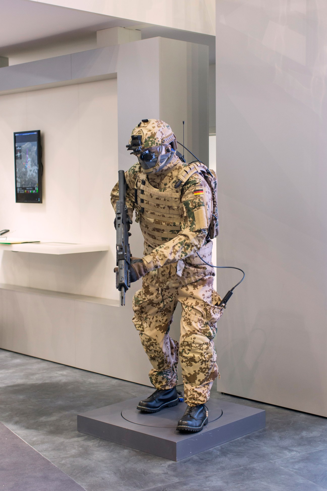 A mannequin dressed in desert camouflage fatigues, tactical gear, and helmet with night vision goggles, holding an assault rifle at the Rheinmetall stand.