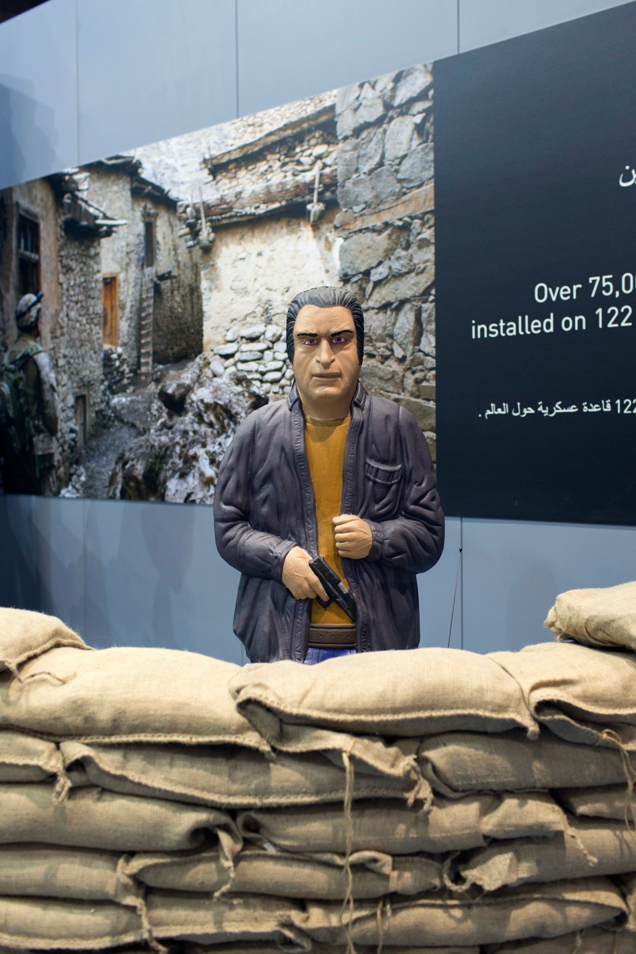 Mannequin figure at Meggitt target training system display with sandbags and conflict backdrop.