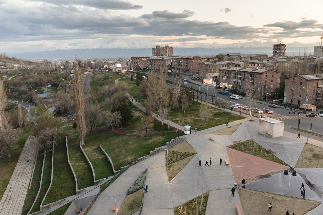 Aerial view of Yerevan's city park with Mount Ararat snow-capped peak visible in the distance beyond Soviet-era apartment buildings.