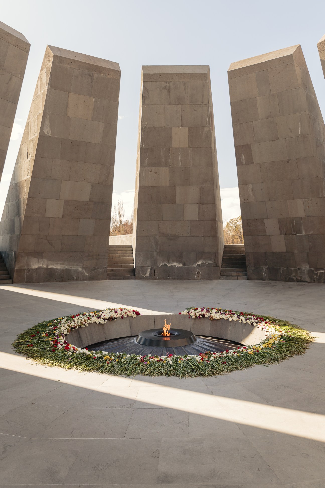 Eternal flame memorial with stone monuments and flower wreaths in Yerevan, Armenia.