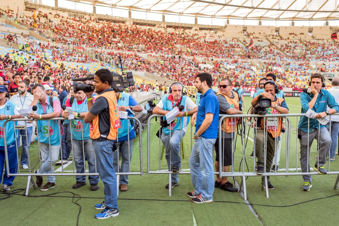 Broadcast journalists and cameramen line the Maracanã stadium field with equipment during a live match transmission.