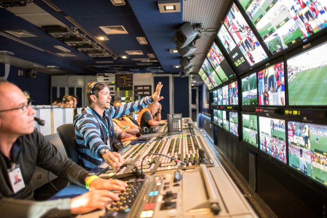 Broadcast technicians operate mixing consoles in a mobile unit during a live football match transmission.
