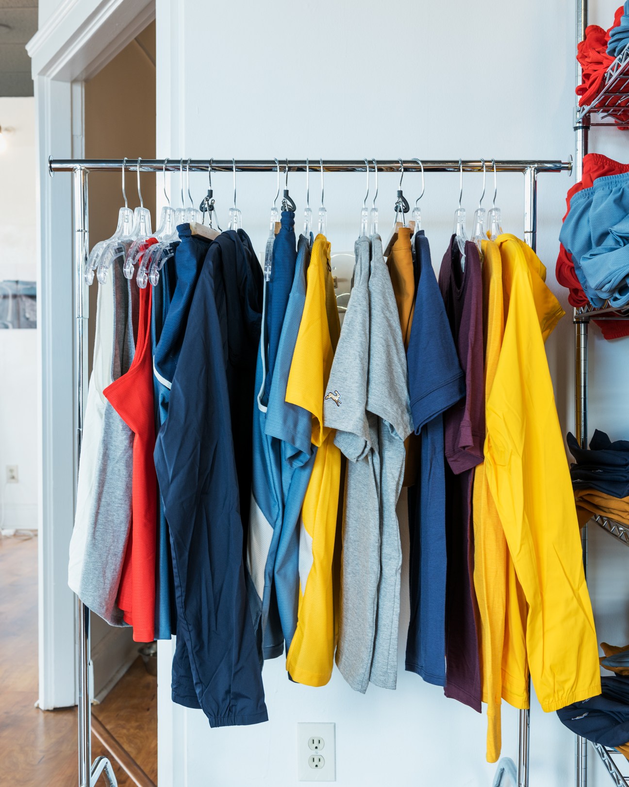 Tracksmith running apparel in various colors hung on a metal rail display.