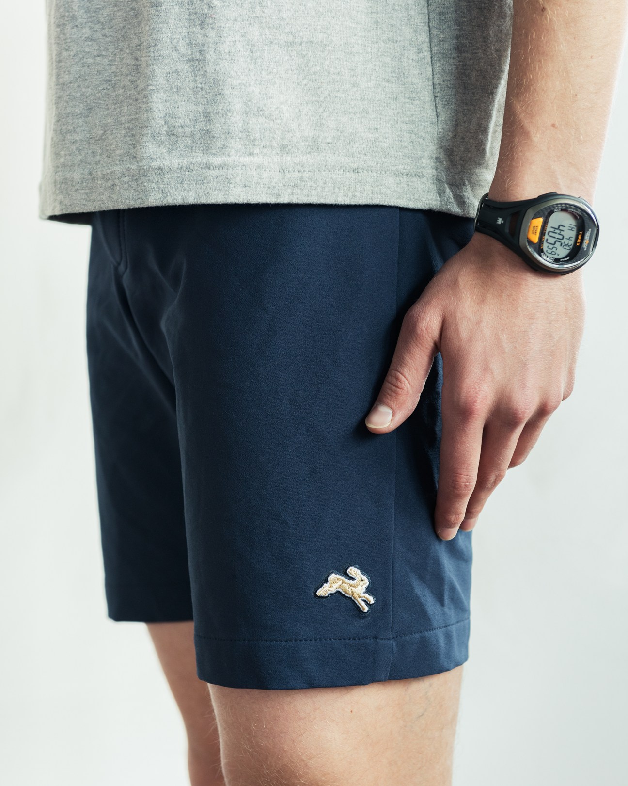 Man wearing Tracksmith Longfellow shorts and gray T-shirt with sports watch.