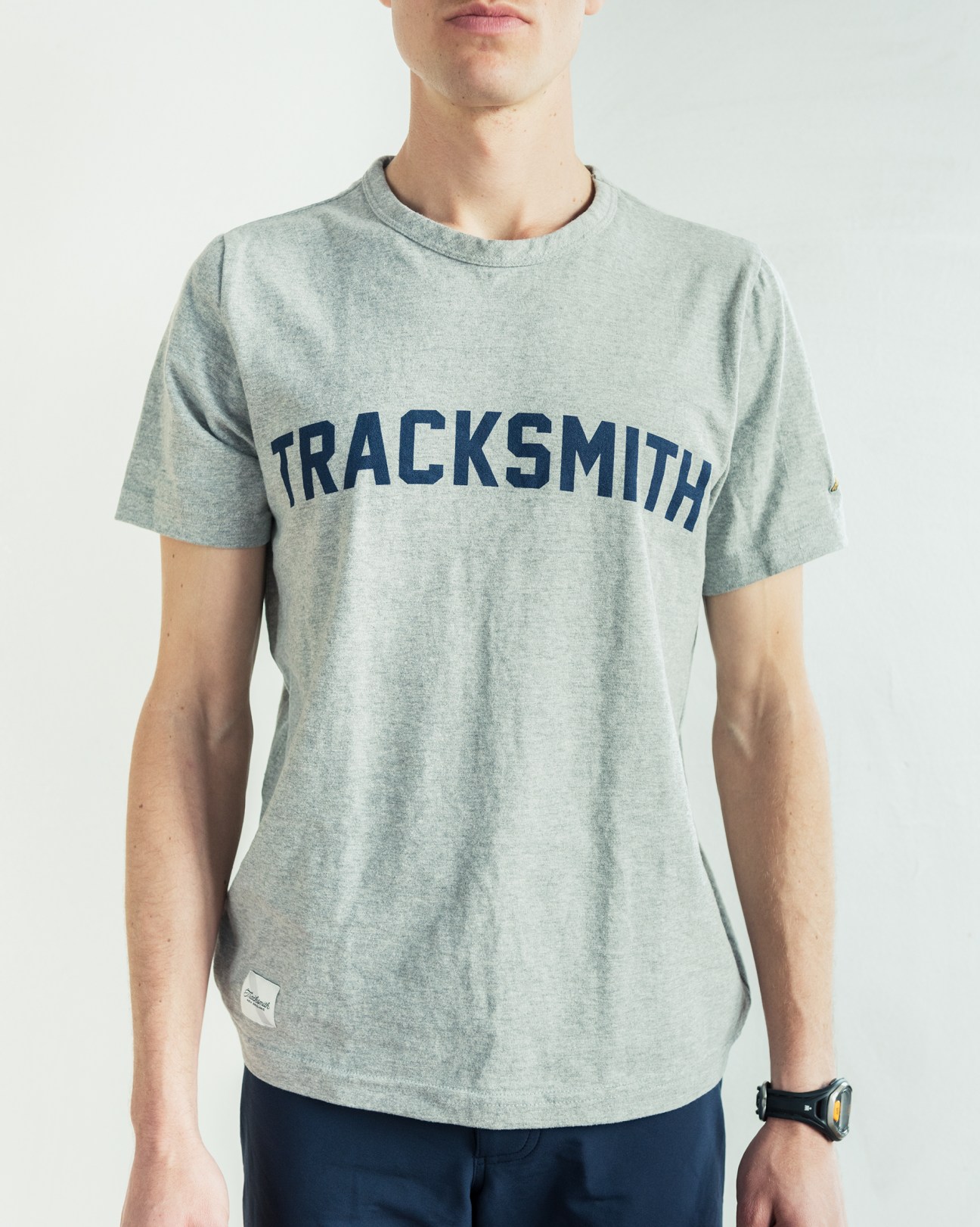 Man wearing gray Tracksmith t-shirt with navy text logo and navy shorts.