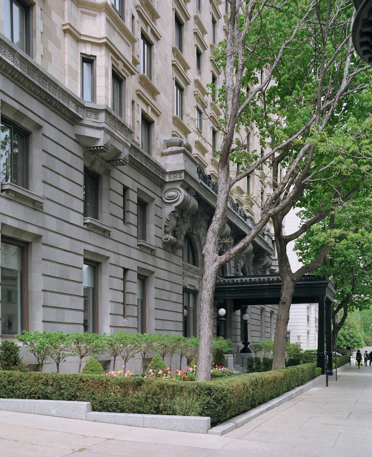 The Linton building entrance with beaux arts granite façade, ornamental mascarons, and a large tree in front garden on Sherbrooke Street West.