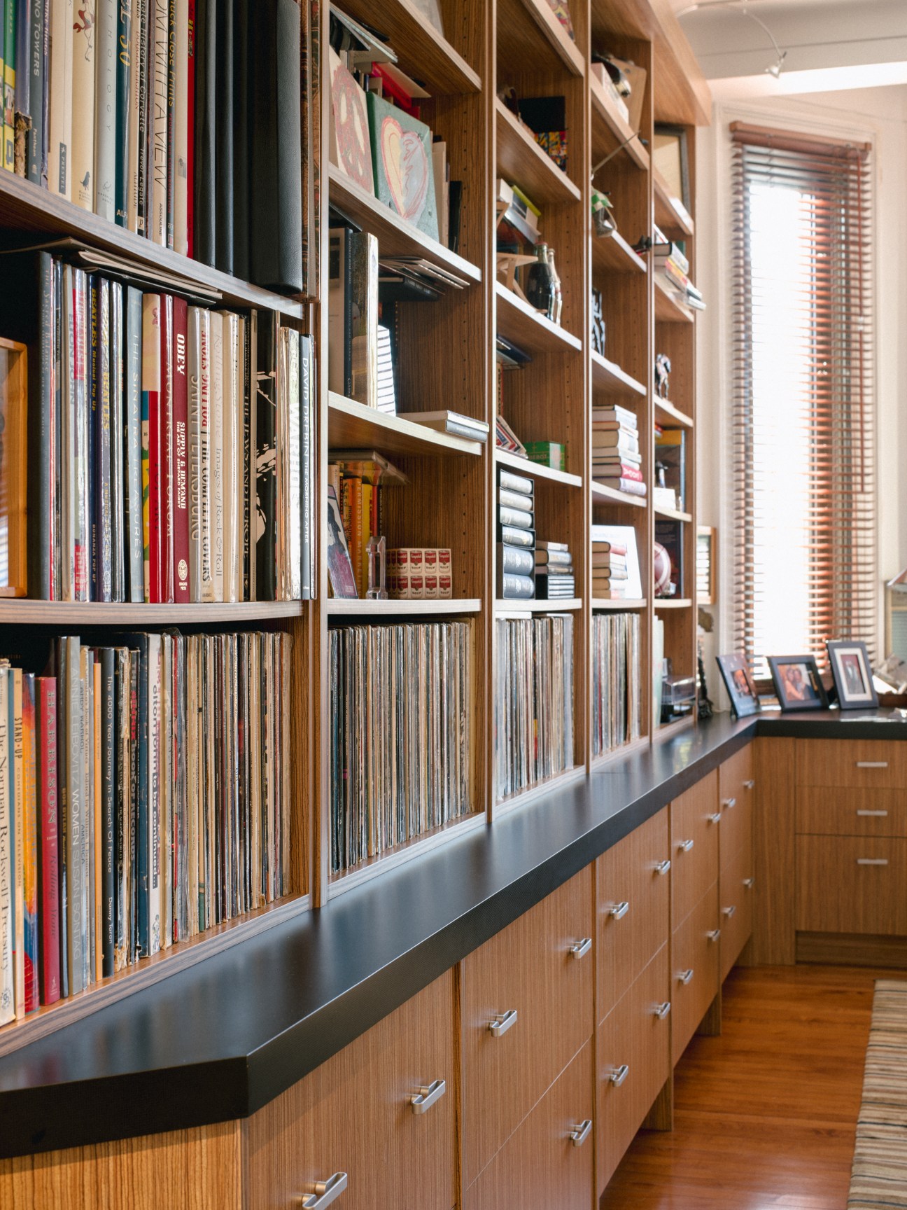 Custom wooden bookcases with metal countertop in an office, displaying books, vinyl records, and decorative items.