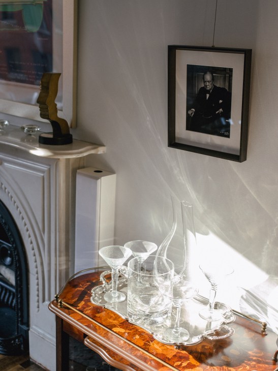 Elegant fireplace mantel with crystal glassware and decanter, framed portrait on wall above.