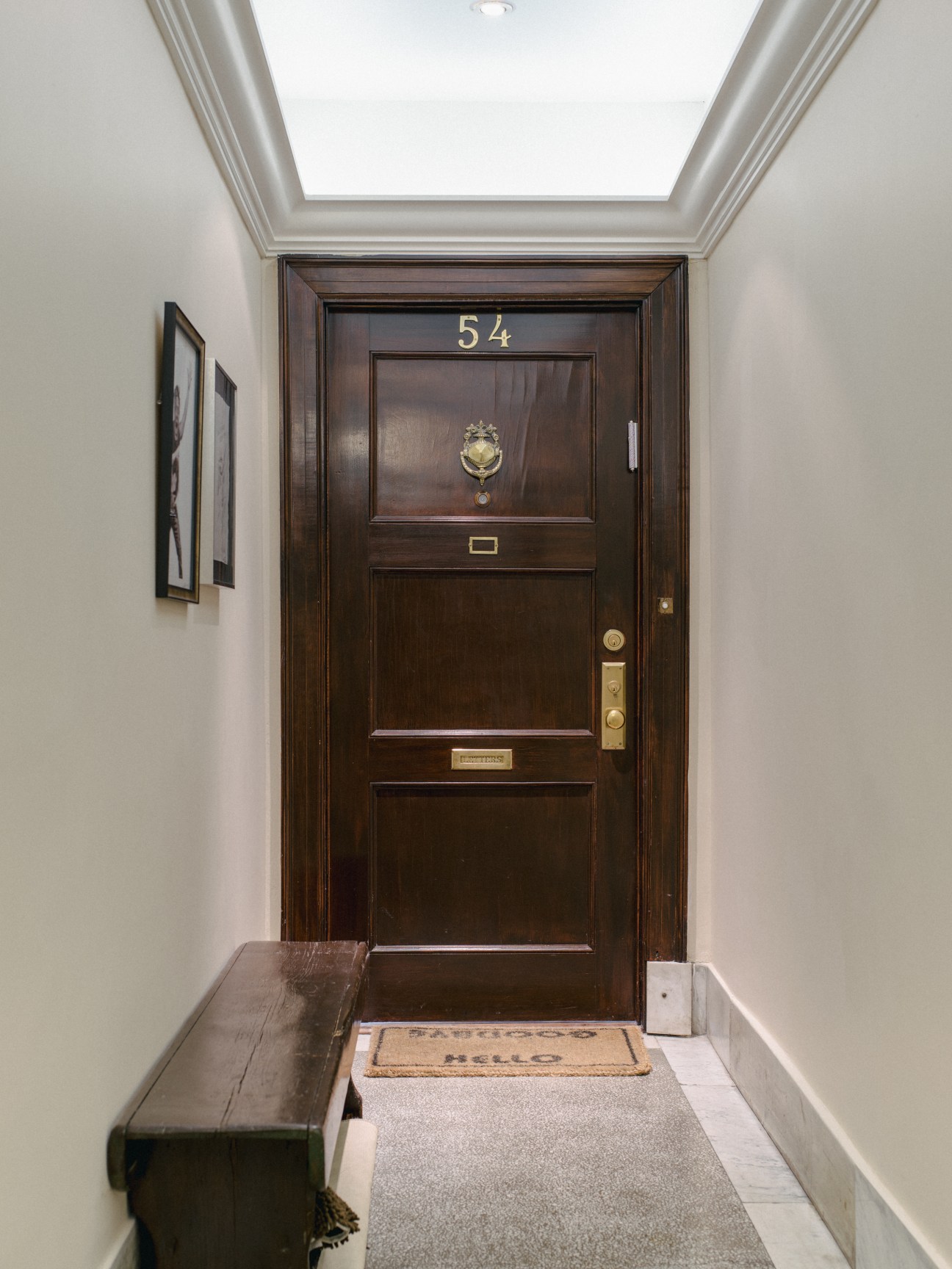 Dark wooden front door numbered 54 with brass door knocker and mail slot in a white-walled entrance hall.