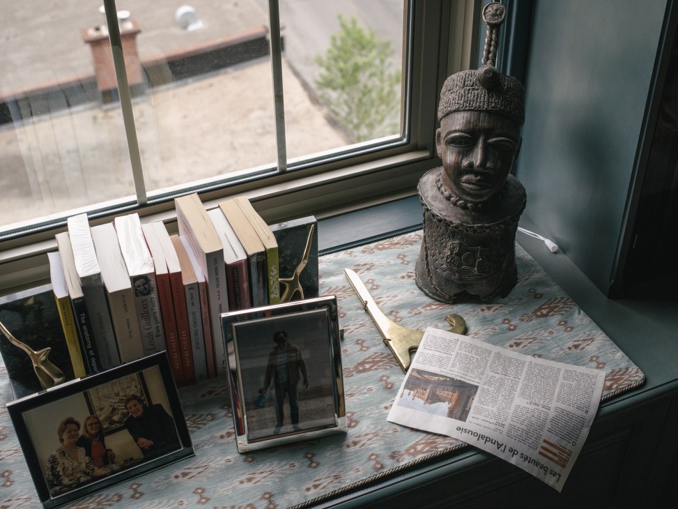 Windowsill display with books, framed photographs, carved wooden bust, newspaper, and decorative objects.