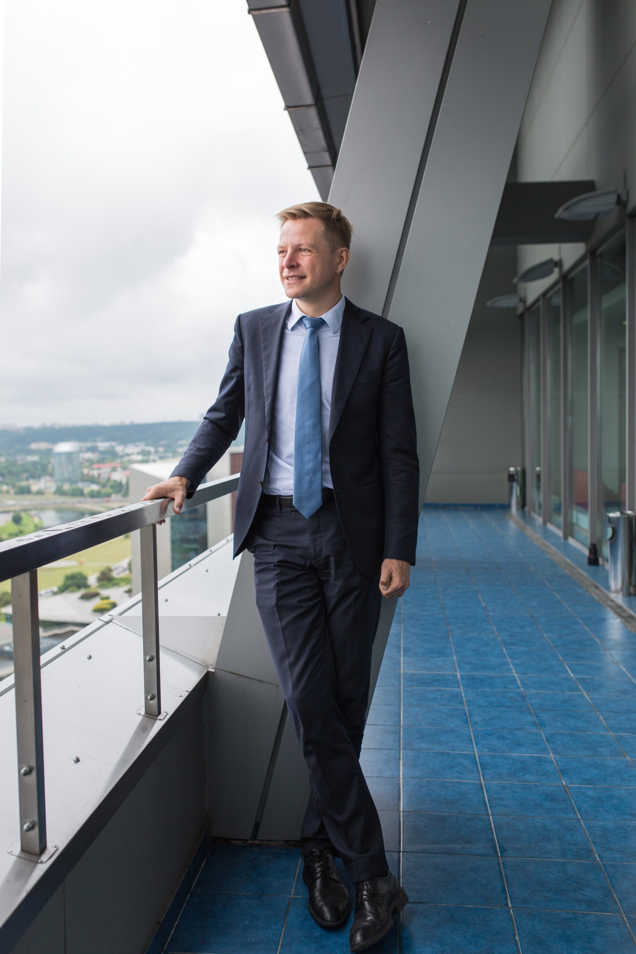 Remigijus Simasius, mayor of Vilnius, stands on a modern building balcony overlooking the city landscape.
