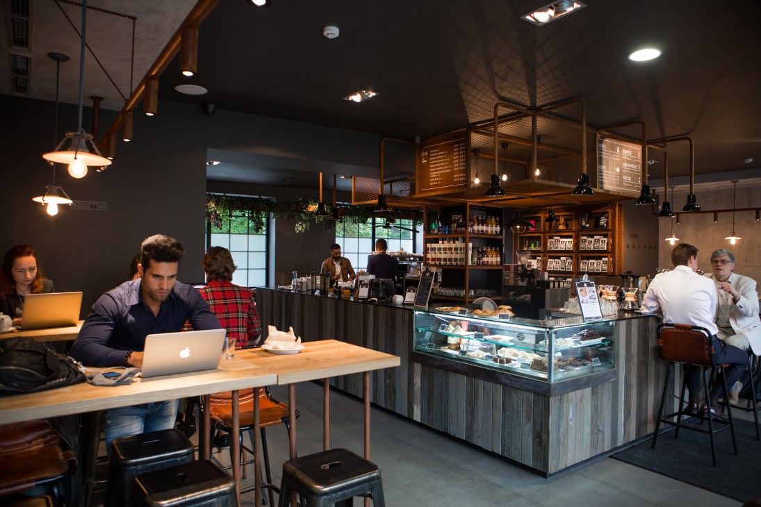 Sviezia Kava coffee bar with customers working on laptops at wooden tables and baristas behind counter