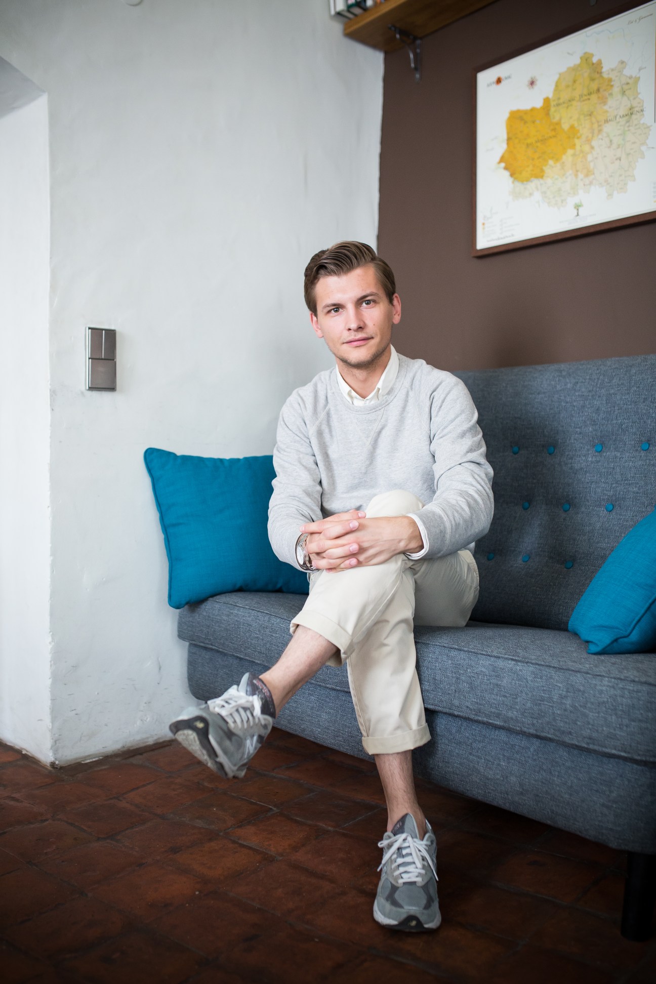 Andrei Maewski, GlobalHRU co-founder, sitting on a gray sofa with blue pillows in an office with a map on the wall.