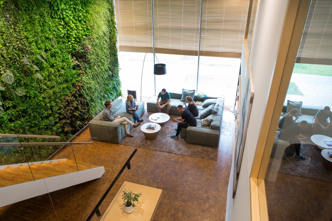 Pixelmator team members sitting on light-colored couches in a modern office lounge with a living green wall on the left side.