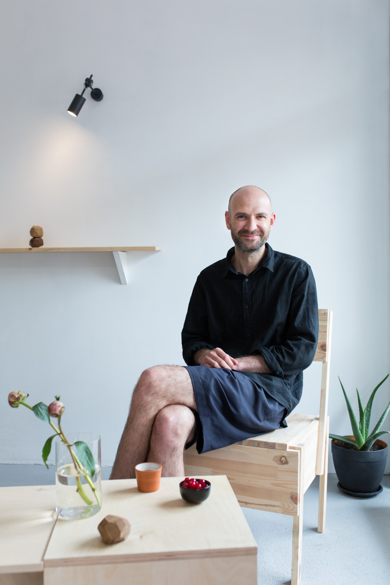 Emanuelis Ryklys, owner of Crooked Nose & Coffee Stories, seated in a minimalist studio setting with plants and design objects.