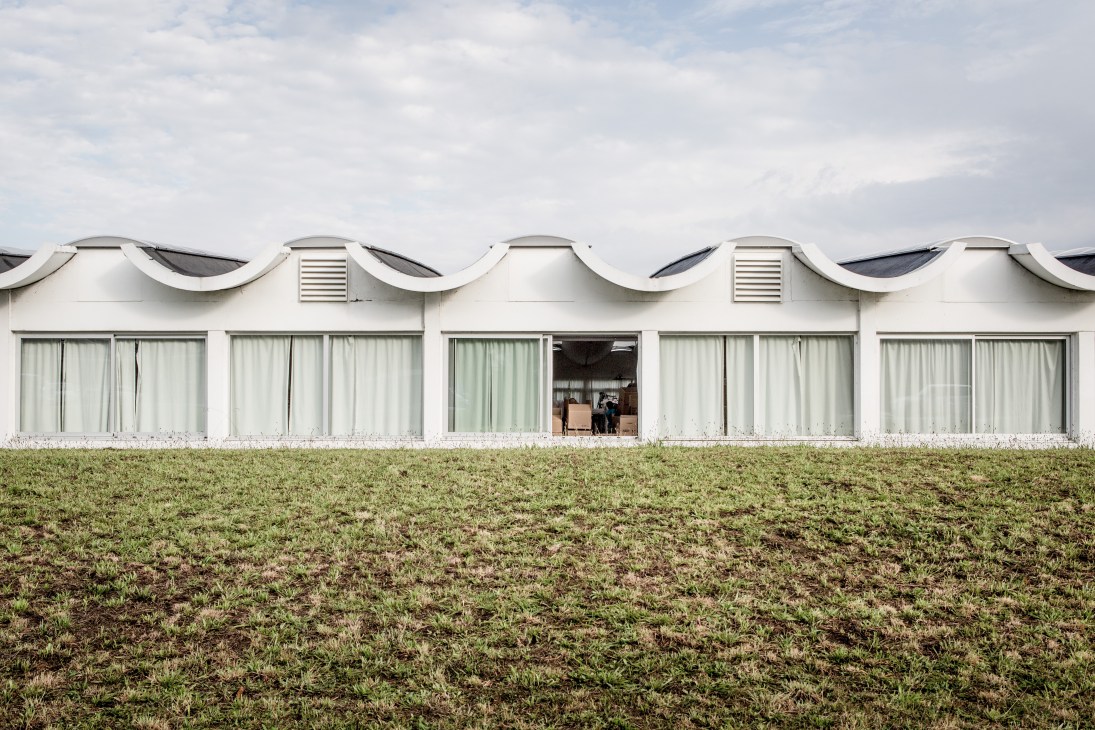 White modernist building with curved roof and large windows set in a grassy field.