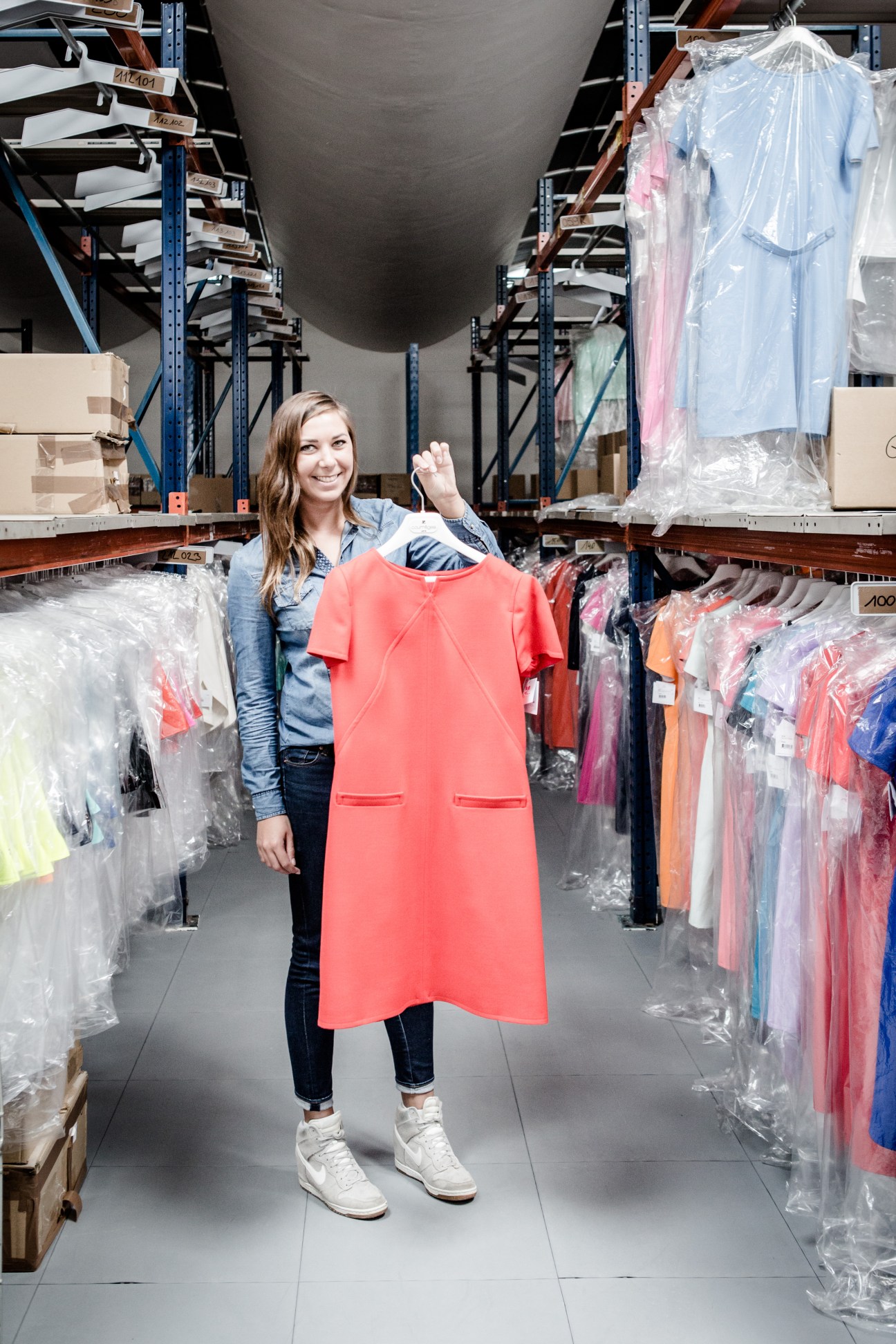 Woman holding a red dress in a warehouse with clothing hanging on racks.