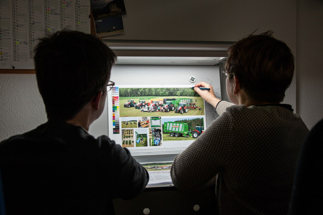 Two people viewing agricultural magazine spreads on a light box in an office.
