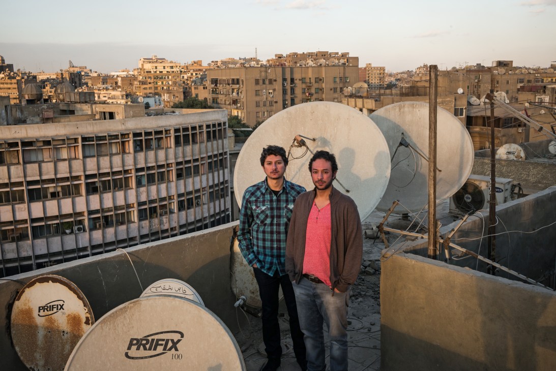 Abdel-Rahman and Tariq Hussein stand on a Cairo rooftop surrounded by water tanks, with the city skyline behind them.