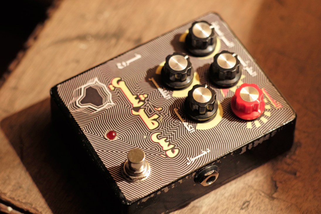 A decorative distortion pedal with black knobs and a red switch on a patterned surface.