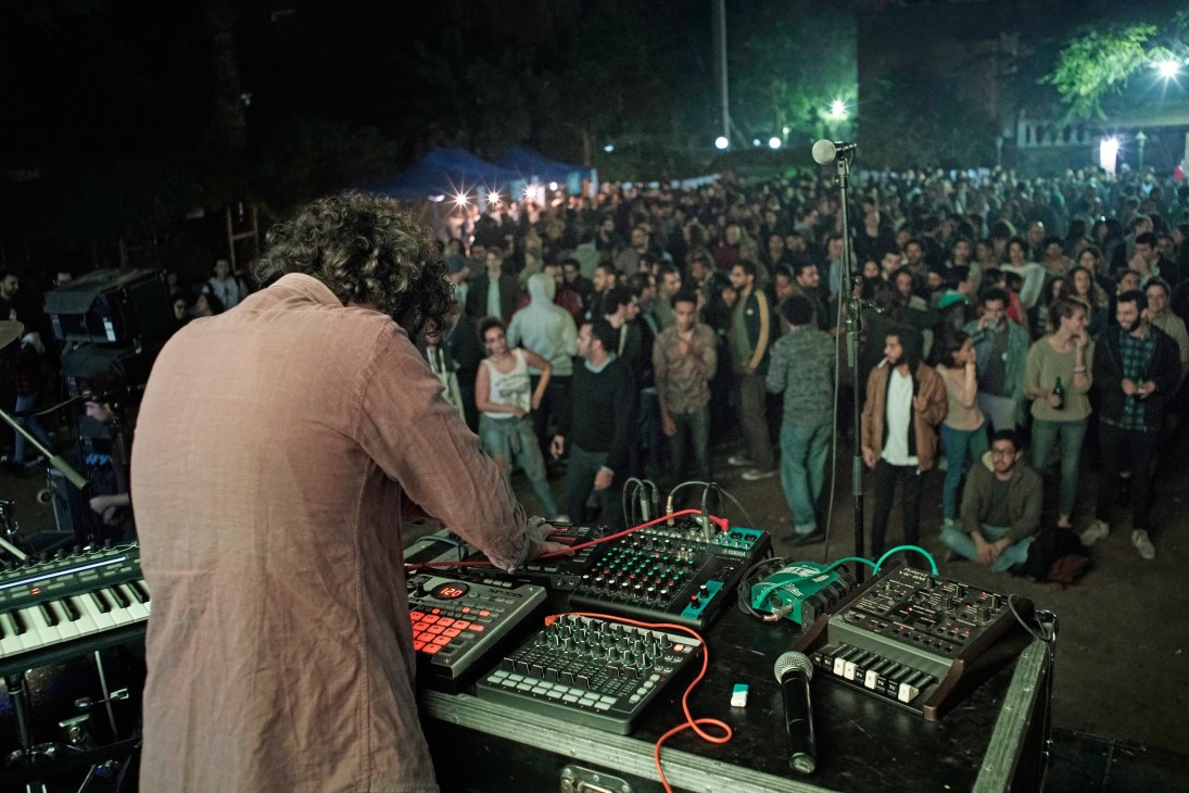 Egyptian musician Maurice Louca performing at DJ equipment with a large crowd gathered at night.