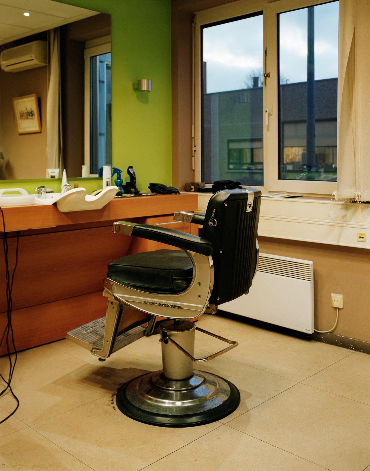 A modern barber shop interior with a vintage barber chair, lime green accent wall, and large windows overlooking the building exterior.