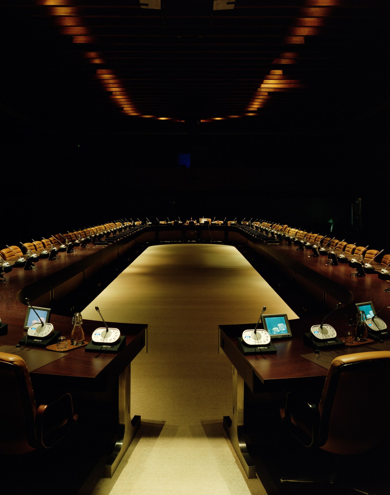 Dimly lit NATO North Atlantic Council room with curved seating arrangement and illuminated central table.