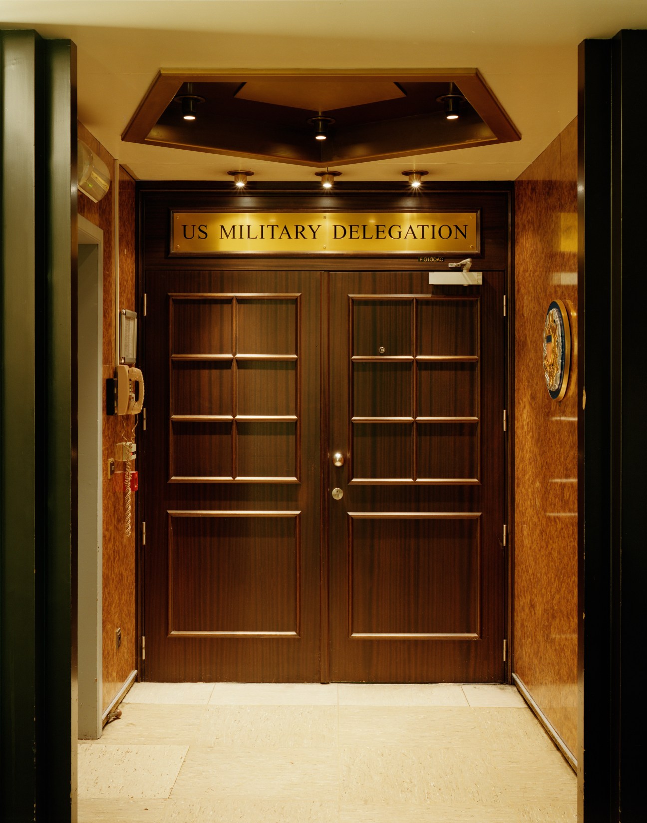 Wooden double doors labeled 'US Military Delegation' with a pentagonal seal on the wall.