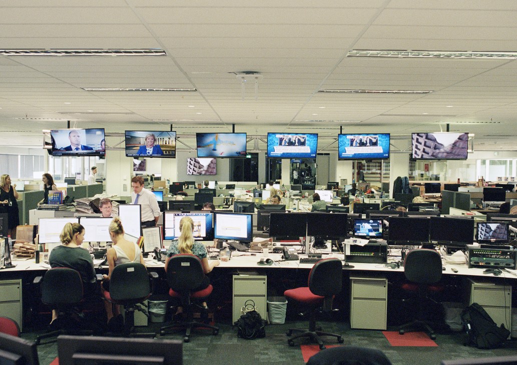The West Australian's converged editorial floor with journalists at desks, multiple computer monitors, and broadcast screens on the wall above.