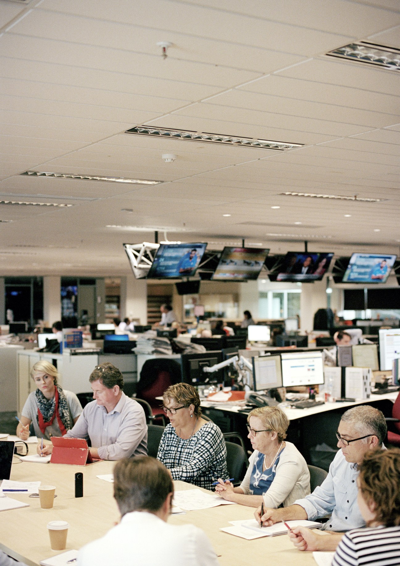 Journalists and editors seated at a table during The West Australian's 11:00 editorial meeting in the newsroom.