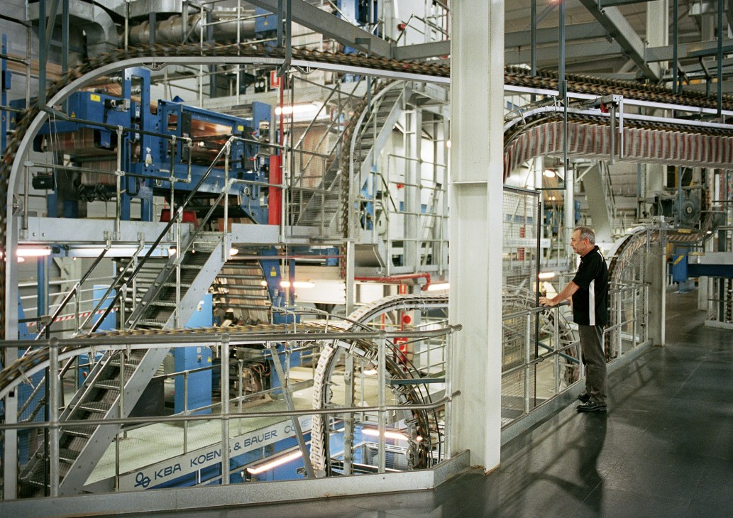 Man in black shirt observing the award-winning Herdsman Print Centre's printing machinery and conveyor systems.