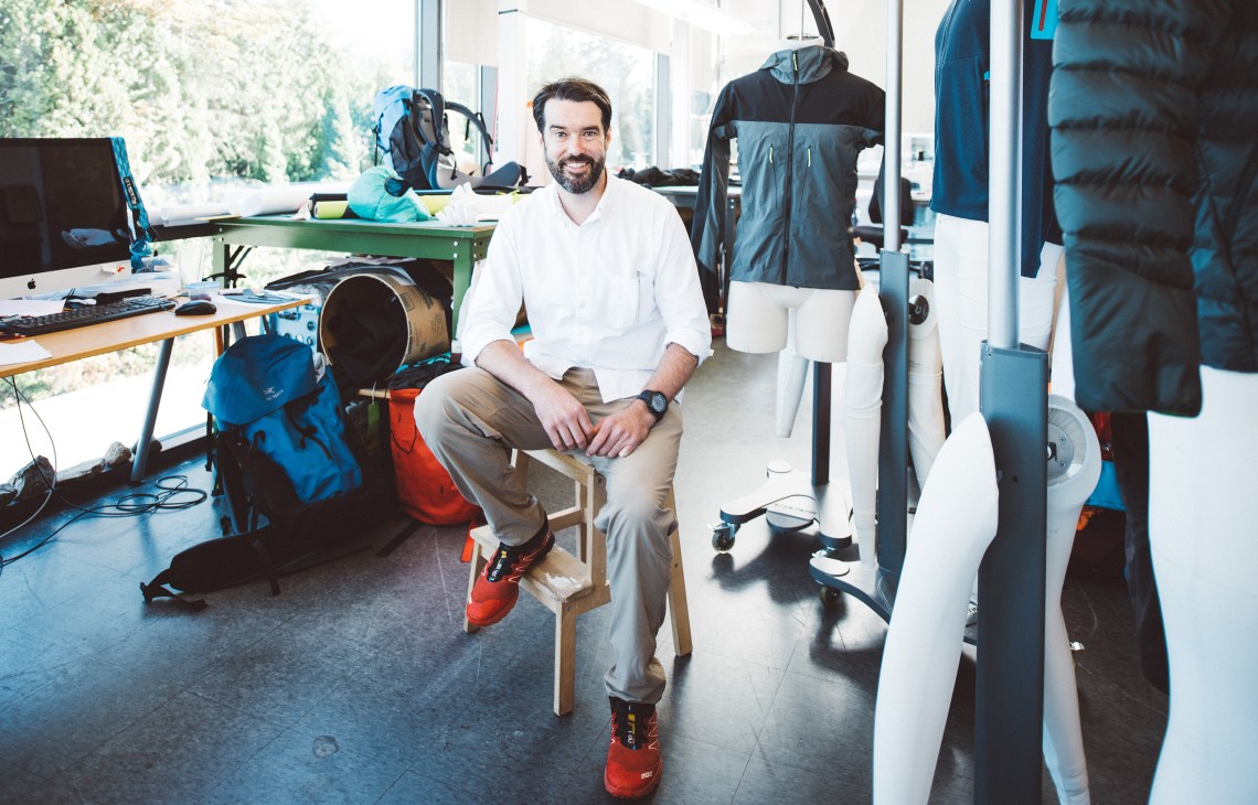 Man sitting in Arc'teryx design studio surrounded by outdoor clothing and equipment samples.