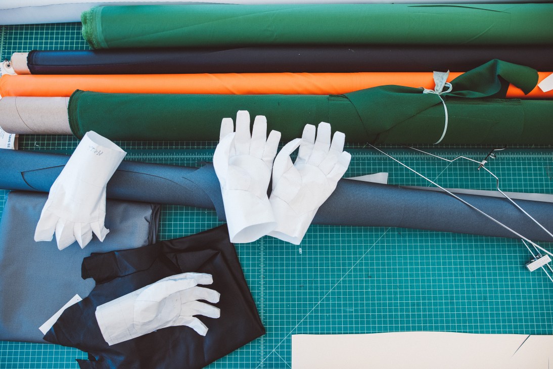 Arc'teryx materials and white gloves on a cutting mat with rolled fabrics and design samples.