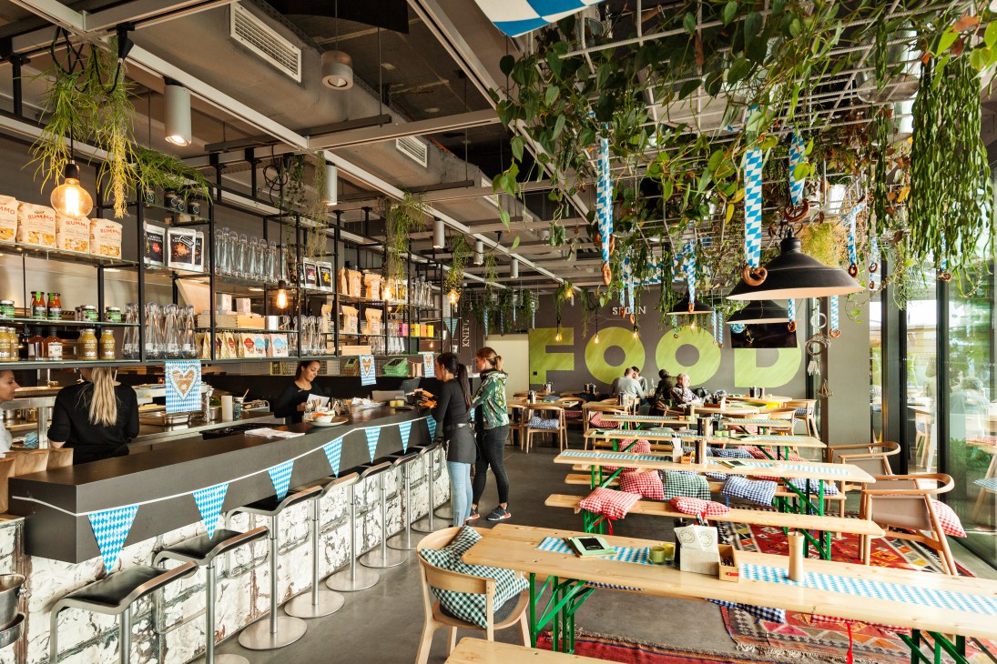 The Dachgarten restaurant interior with Bavarian bunting, hanging plants, counter seating and dining tables set for lunch service.