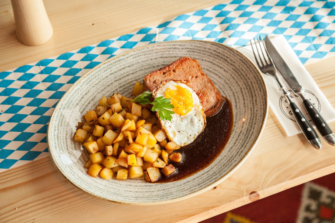 Traditional German dish with meat, fried potatoes and fried egg on blue-white checkered tablecloth at Dachgarten restaurant.