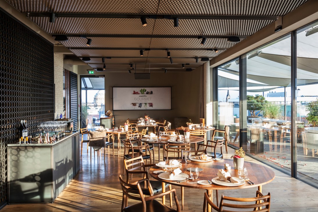Scandinavian-inspired dining room at Opus V restaurant with wooden chairs, set tables, and city views through large windows.