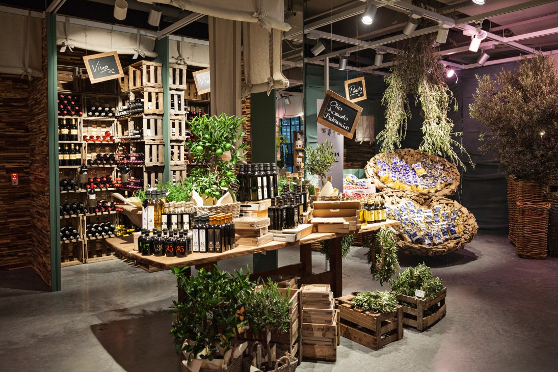 Italian delicatessen display at Engelhorn with wine bottles, olive oil, fresh produce and plants.