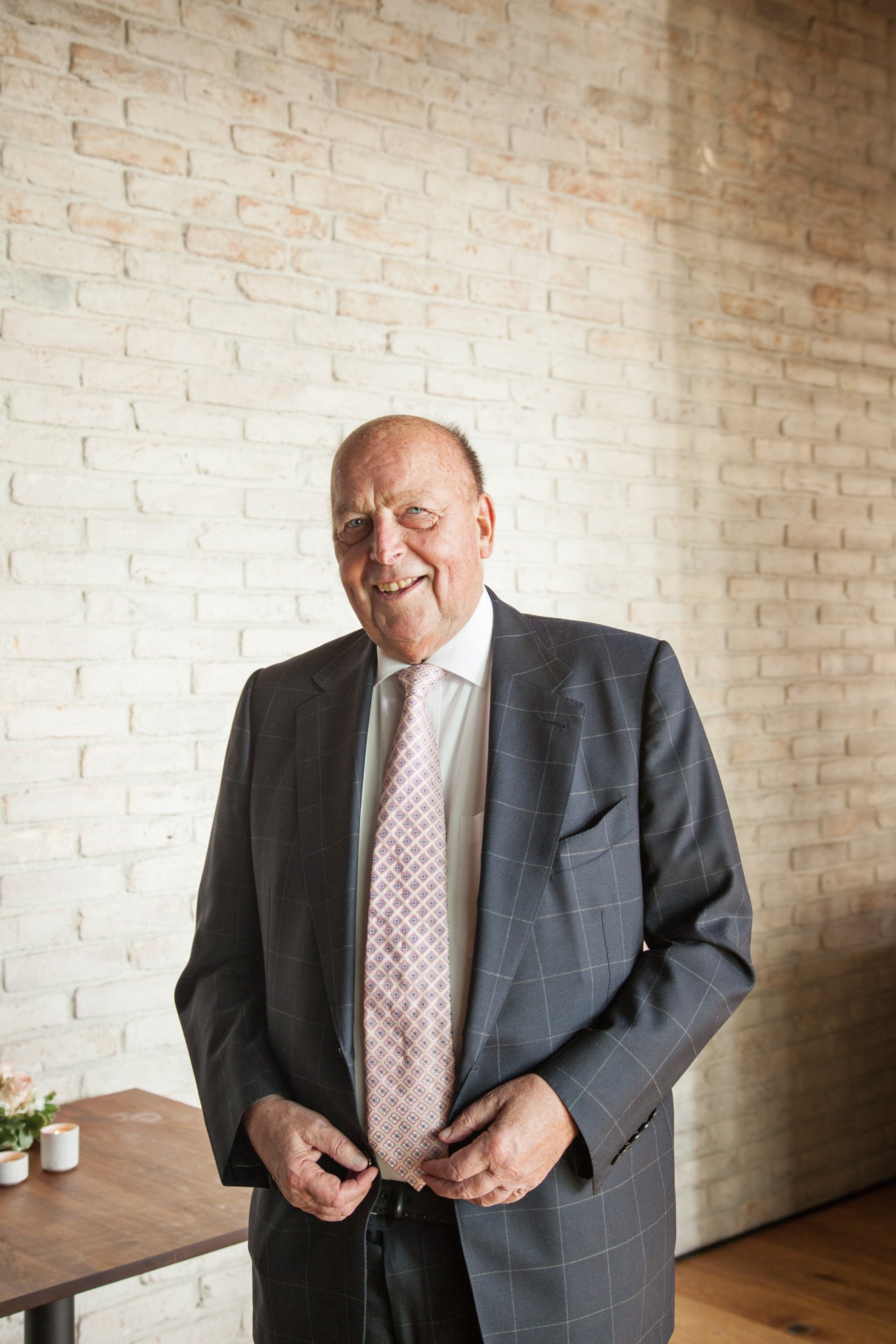 Richard Engelhorn stands in a tailored suit against a white brick wall in an office setting.