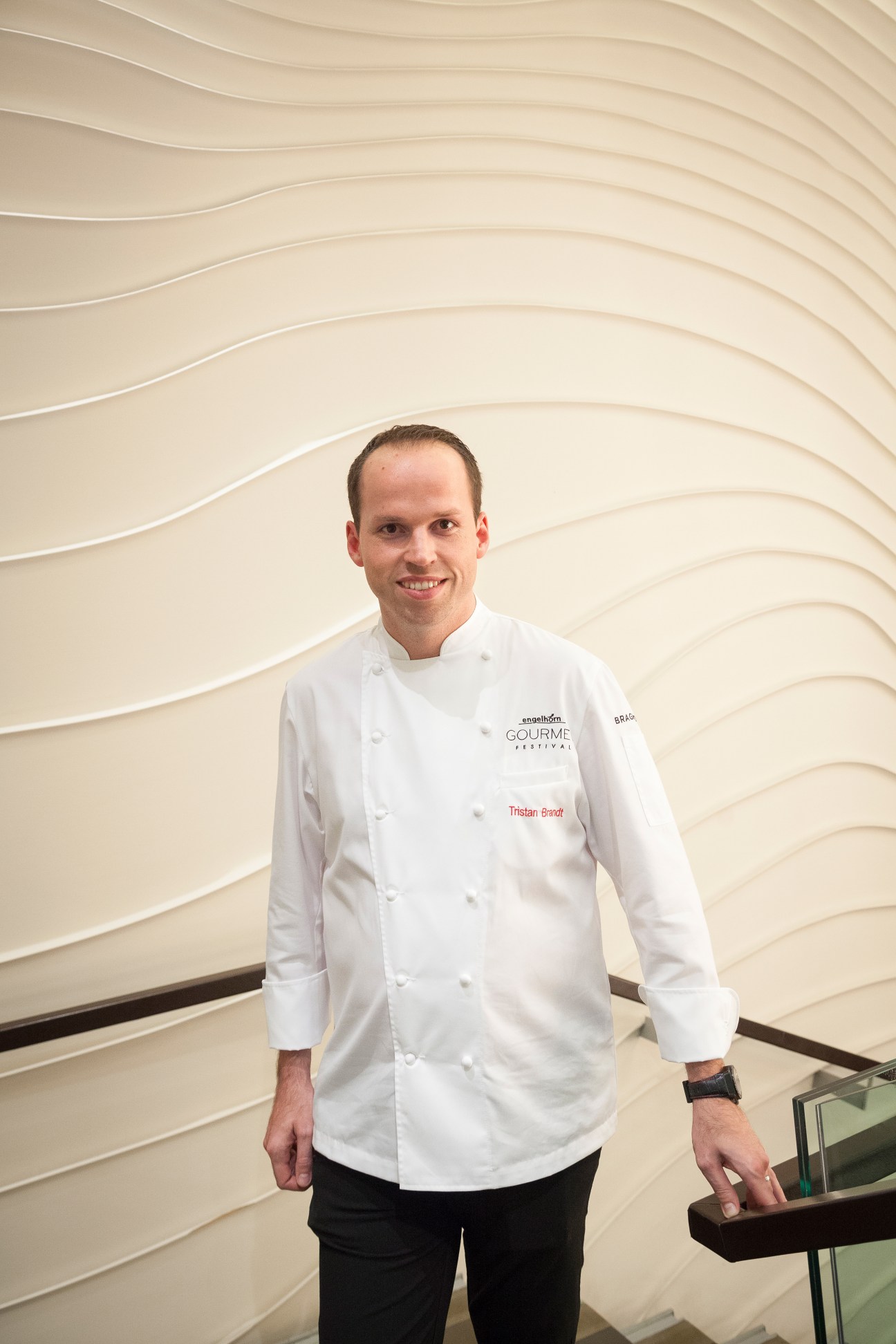 Chef Tristan Brandt in white chef's coat standing against wavy beige wall